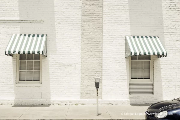 White wall with shopping windows and a car part parked in front of a meter