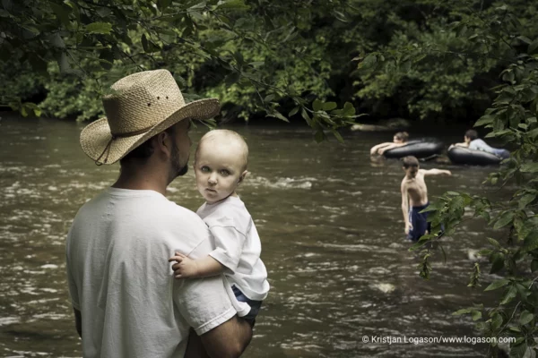 Man standing by the river in The Sinks in Tennessee holding a child in his arms and the child is facing the camera