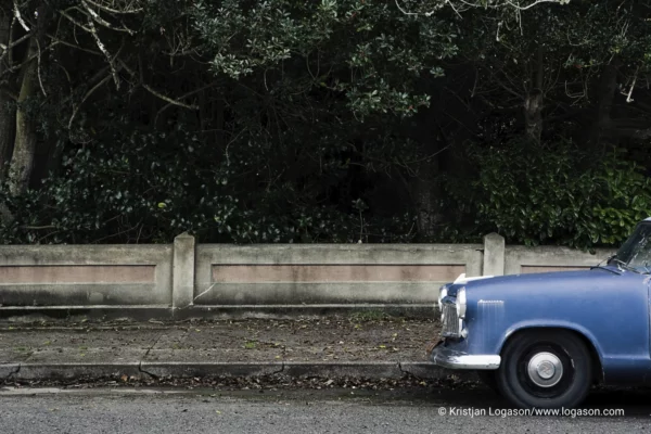 Part of a blue car parked in front of a concrete fence in Ferndale, California