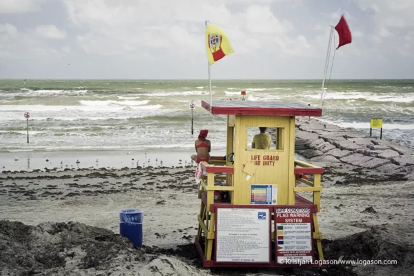 Lifeguard in a red swim suite sitting in a yellow lifeguard tower