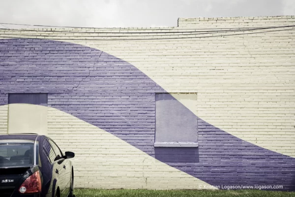 Car part in front of a yellow and purple brick wall of a building in New Iberia